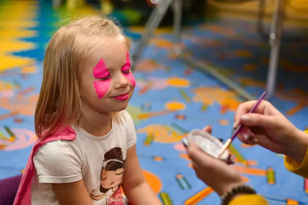 The animator paints a drawing on the face of a little girl at a party.
