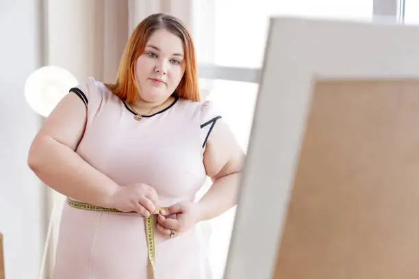 I am fat. Nice red haired woman measuring her waist while wanting to lose her weight