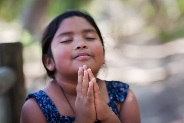 A native young girl with hands together in prayer, in an outdoor setting praying to God with a subtle smile. stock photo