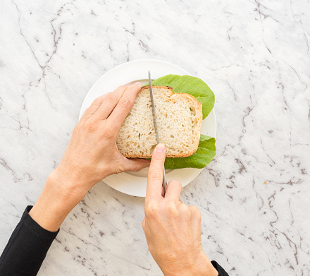 High angle view of hands cutting salad sandwich with knife against grey marble background