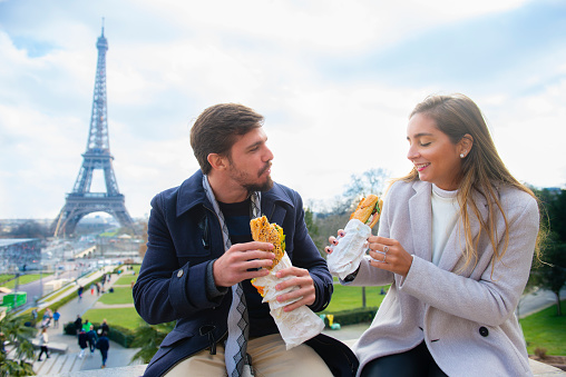 A couple eats french sandwiches in the baguette bread before visit the Eiffel tower