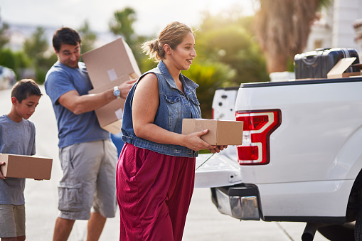 hispanic family moving boxes out of pickup truck into house during the day