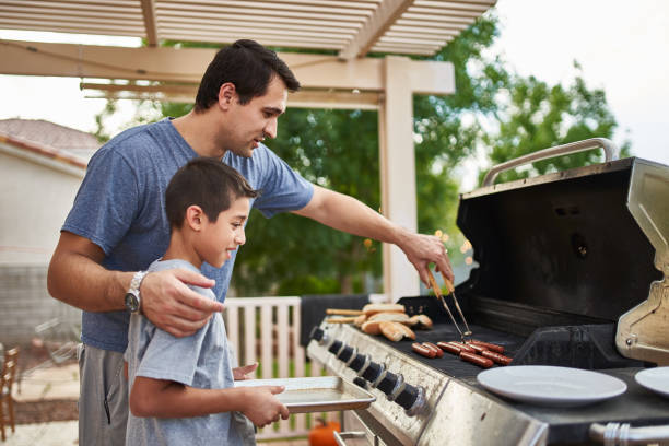 padre enseñando a su hijo cómo asar hot dogs y unir - cocido a la parrilla fotos fotografías e imágenes de stock