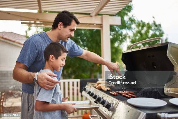 Father Teaching Son How To Grill Hot Dogs And Bonding Stock Photo - Download Image Now