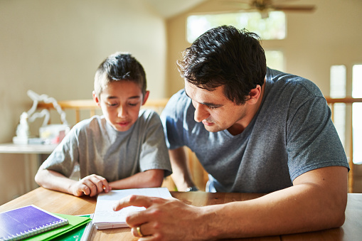 father helping son with homework on table at home during the day