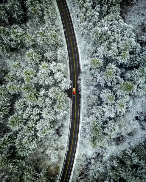 A drone view directly above a snowplow on a Pacific Northwest road surrounded by trees with a dusting of snow