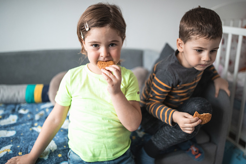 Two kids on the bed eating cookie