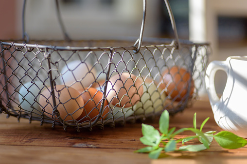 Closeup of rustic wire basket of fresh eggs on the table in natural morning light