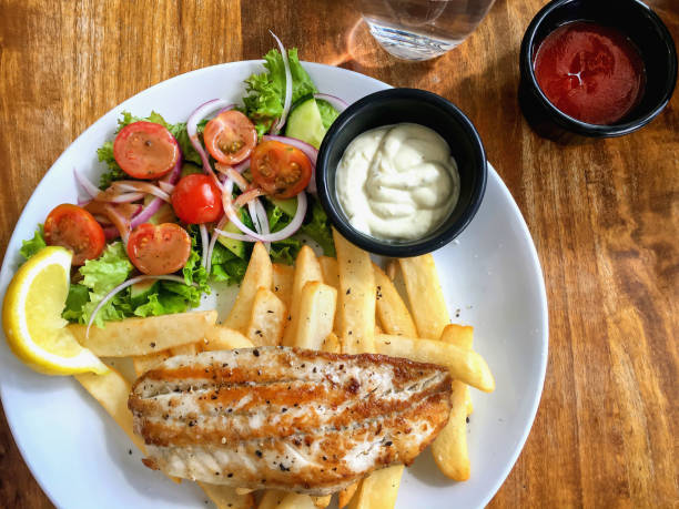 Close up shots of fresh fish and chips with fries, salad and tartar sauce on table