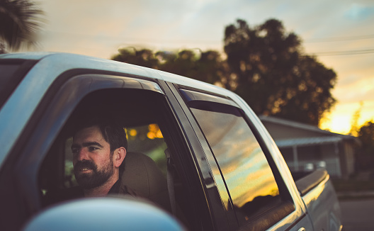 Handsome man in his 30’s with a rugged looking beard in a truck with the evening sunset reflected in the window. Cheerful candid and beautiful nature
