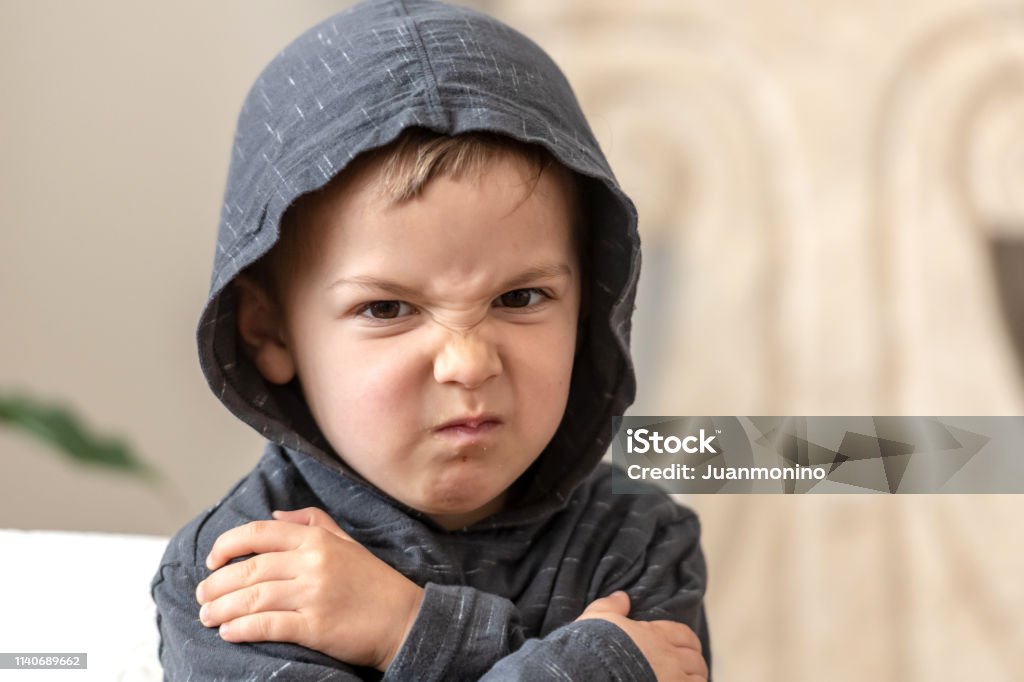 very upset three years old boy looking at the camera very upset three years old boy looking at the camera wearing a hoodie Anger Stock Photo