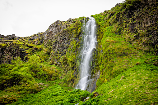 Small waterfall by Seljalandsfoss, Iceland with white water falling off cliff top long exposure in green mossy summer rocky landscape