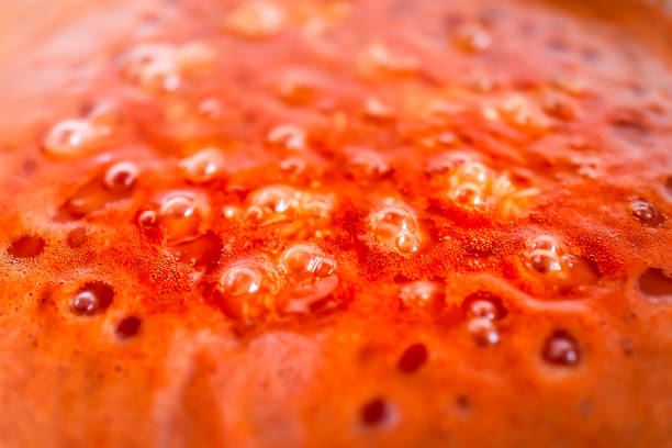 Closeup of red orange tomato soup or sauce boiling bubbling in pot macro closeup showing abstract detail texture surface Closeup of red orange tomato soup or sauce boiling bubbling in pot macro closeup showing abstract detail texture surface boiling photos stock pictures, royalty-free photos & images