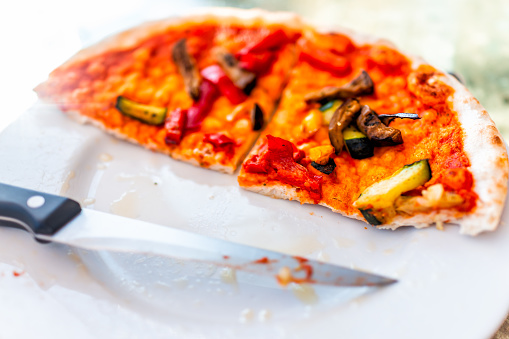 Closeup of fresh crust homemade vegan sliced knife pizza half on table in Italy with red tomato sauce vegetables eaten