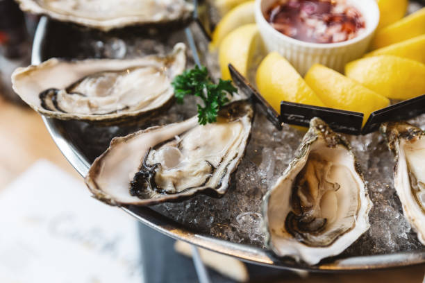 da vicino ostriche fresche e molti tipi di ostriche fresche servite in vassoio rotondo con fetta di limone e salsa piccante. - oyster foto e immagini stock