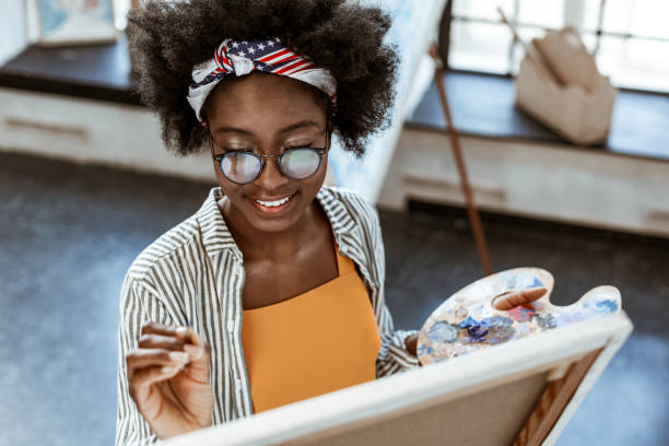 Beaming artist with nice makeup smiling while painting