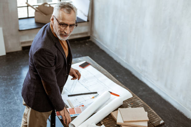 istock Grey-haired experienced interior designer standing near sketches 1140711107