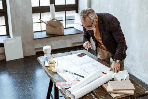 istock Grey-haired interior designer wearing jacket holding compasses 1140711115