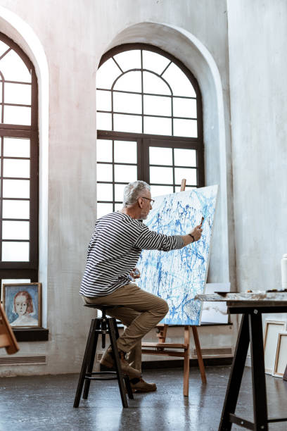 istock Grey-haired artist painting on canvas in spacious workroom 1140711127
