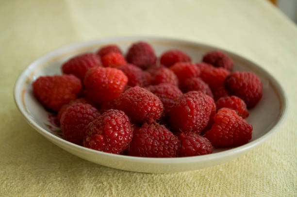 istock Ripe raspberries are laying on the white plate which is standing on the table covered with yellow tablecloth 1140719915