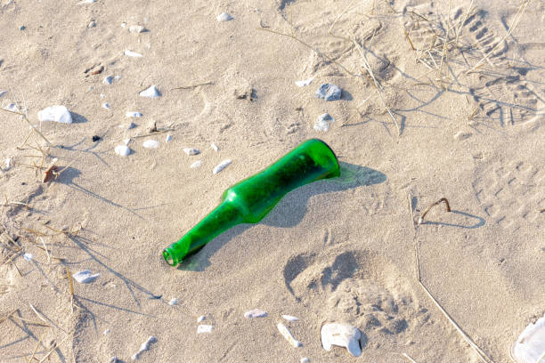 boot prints on the sand beach and man-thrown green glass bottle. concept of environmental pollution.