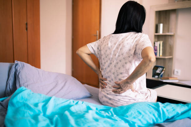 ビギナーズとベッドの上に座っているシニア女性 - lower back pain ストックフォトと画像