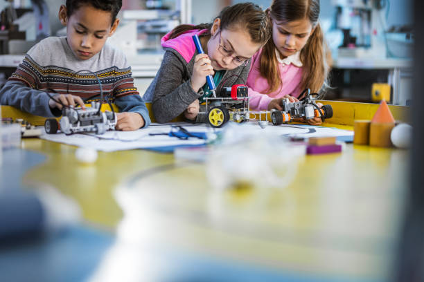 Group of small kids working on robots on robotics class. Three little friends making futuristic robots in laboratory. Focus is on girl in the middle. school science project stock pictures, royalty-free photos & images