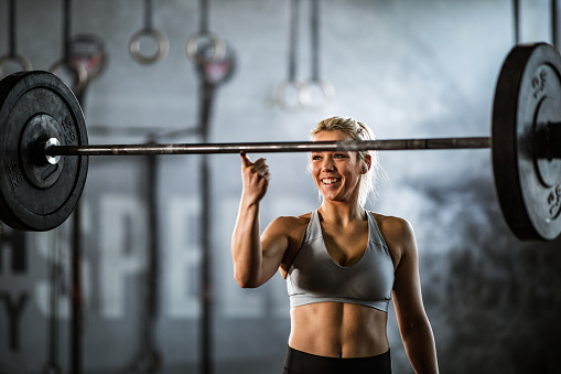 Happy athletic woman holding barbell on her index finger in a health club.