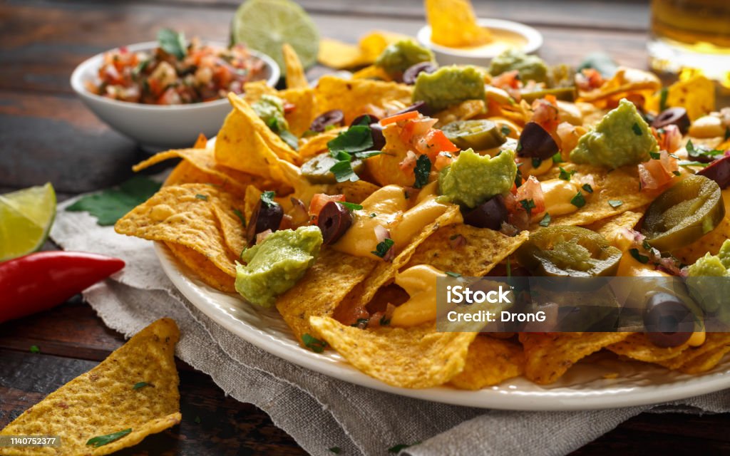 Mexican nachos tortilla chips with olives, jalapeno, guacamole, tomatoes salsa, cheese dipand beer. Mexican nachos tortilla chips with olives, jalapeno, guacamole, tomatoes salsa, cheese dipand beer Nacho Chip Stock Photo
