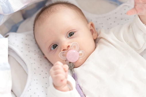 Portrait of cute baby girl with pacifier lying in her crib