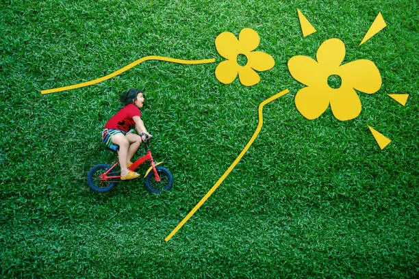 Rear View of a Happy Asian Kids. Girl on Bicycle Lay Down at Green lawn in Spring or Summer Day. Excited Asian Children in her Outdoor Activity