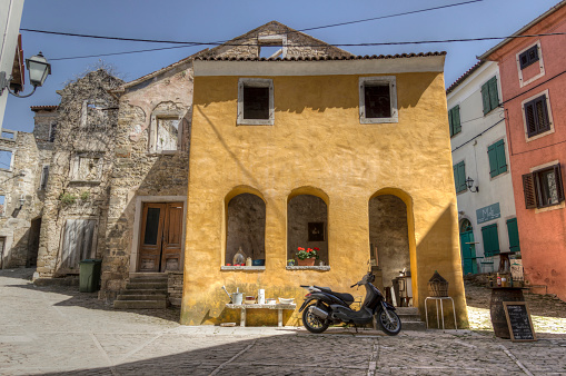Central Istria, Croatia, April 19th 2018: Scooter parked in front of an old yellow house at the corner of two streets in the ancient town of Oprtalj.