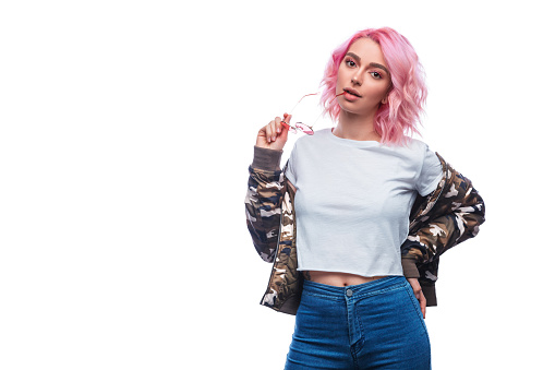 Pretty modern woman with pink dyed hair wearing casual attire and posing with sunglasses isolated on white background