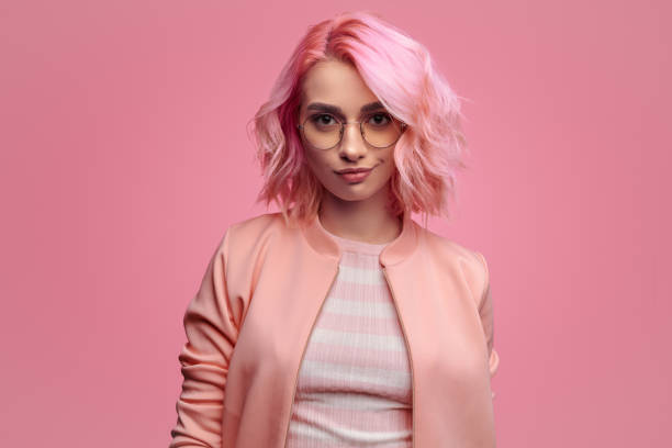 Confident trendy woman in pink outfit Pretty stylish hipster woman with pink hairstyle wearing jacket with glasses and looking provocatively at camera on pink background multi coloured glasses stock pictures, royalty-free photos & images