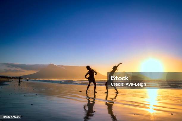 Two African Women Dancing On The Beach At Sunset With Table Mountain And Cape Town In The Background Milnerton Beach Cape Town South Africa Stock Photo - Download Image Now