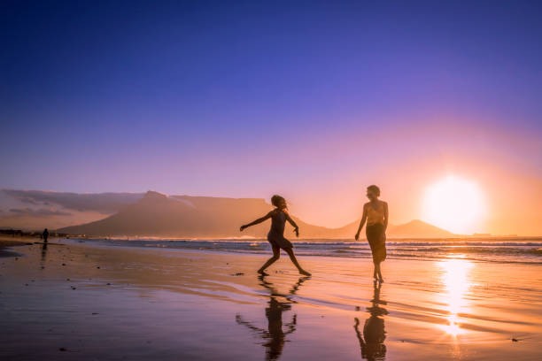 Two African women dancing on the beach at sunset, with Table Mountain and Cape Town in the background, Milnerton Beach, Cape Town, South Africa stock photo