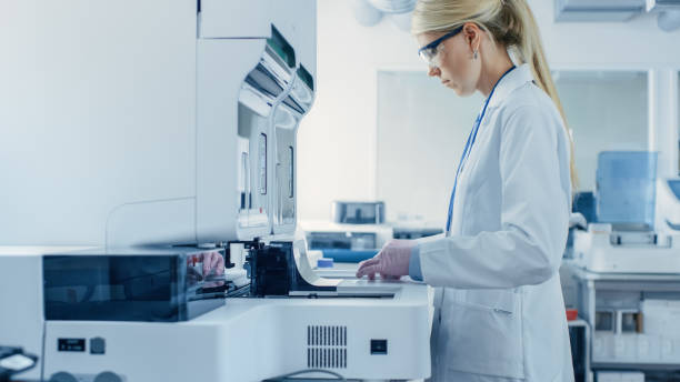 chercheur de recherche femelle mettant des tubes d’essai avec des échantillons de sang dans la machine médicale d’analyseur. scientifique travaille avec l’équipement médical moderne dans le laboratoire pharmaceutique. - scientist research test tube lab coat photos et images de collection