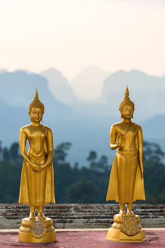 Golden small statues of Buddha in the Wat Tham Suea Tiger cave temple on the background of the silhouettes of the mountains in Thailand
