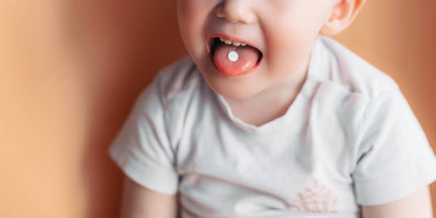 Selective focus at a white pill on a tongue of small toddler baby boy stock photo