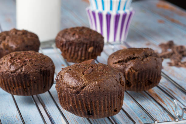 Chocolate Muffins Freshly baked chocolate muffins cooling on a wire rack. A glass bottle of milk and purple and blue striped baking cups sit on a blue wood table behind the muffins. Chocolate Chip Muffin stock pictures, royalty-free photos & images