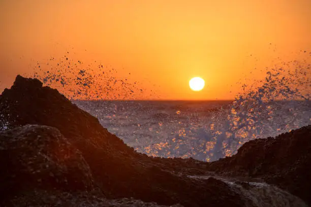 Sea waves crushing and splashing on the rocks on a tropical beach, in beautiful warm sunset light