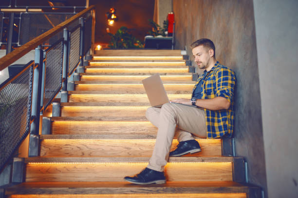 istock Serious Caucasian handsome freelancer in plaid shirt using laptop while sitting on the stairs in cafe. 1140813080