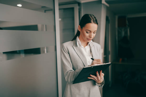 femme d’affaires caucasienne réussie dans l’usure formelle restant au lobby dans l’entreprise et écrivant sur le presse-papiers. certaines personnes rêvent de succès tandis que d’autres se réveillent et travaillent. - central europe photos photos et images de collection