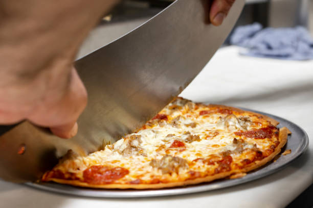 Chef cutting a pizza with a mezzaluna in a restaurant. Chef cutting a pizza with a mezzaluna in a restaurant.  Close up side view.  Hands only visible. mezzaluna stock pictures, royalty-free photos & images