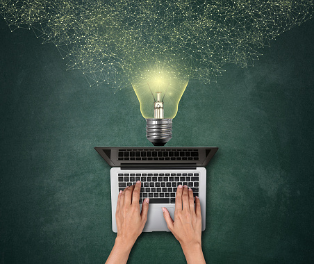 Directly above of a man's hand using laptop with lightbulb