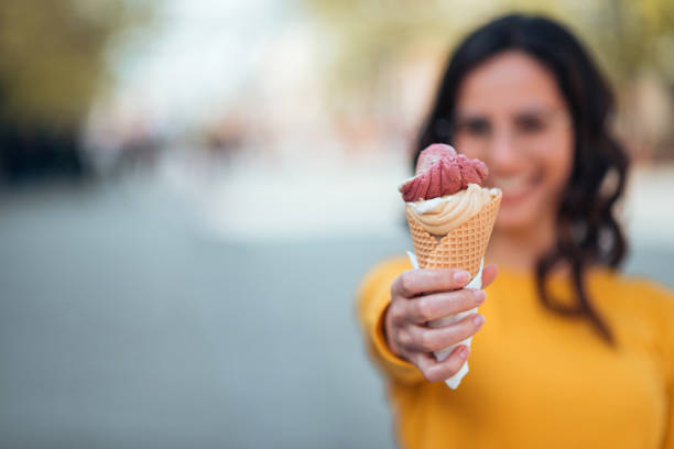 istock Girl holding ice cream cone toward camera outdoors, focus on the foreground, copy space. 1140825536