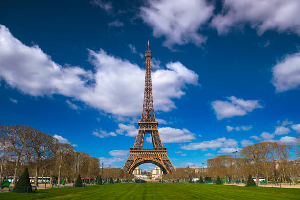 Girl's hand holding heart with french flag colors. Heart is on background of  famous Eiffel Tower, blue sky, clouds, sun. Love, Paris, France, travel concept.