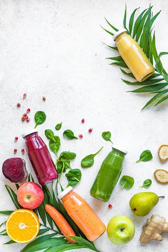 Detox food and clean eating concept. Various smoothies or juices in bottles and ingredients on white, top view, copy space.