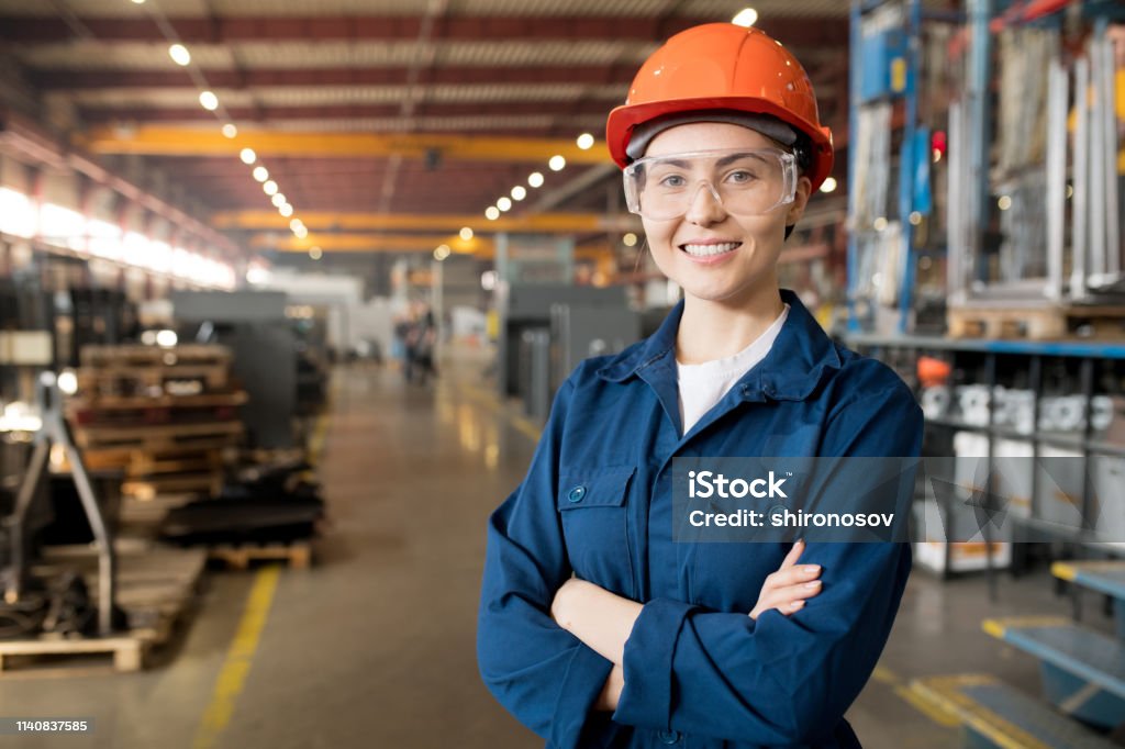 Young controler Young smiling female technician in blue uniform, protective eyeglasses and helmet working in modern factory Occupation Stock Photo