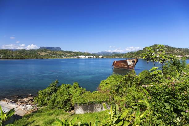 Baracoa Bay Cuba Landscape and El Yunque Mountain on the Horizon Landscape View of Baracoa Bay with Old Rusted Ship and Distant El Yunque Landmark Tabletop Mountain on East Coast of Cuba baracoa stock pictures, royalty-free photos & images